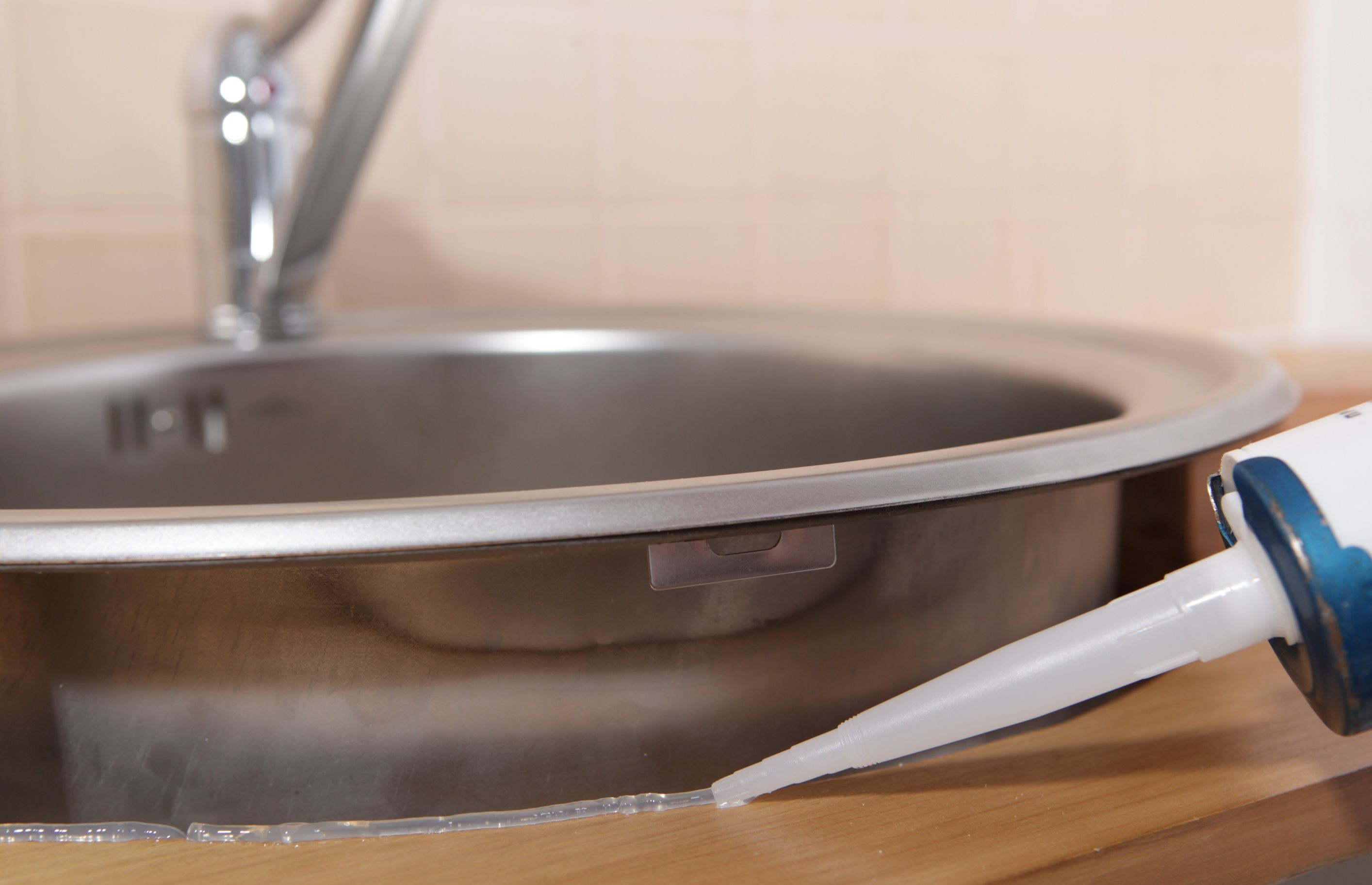 Zbliżenie na stalową umywalkę i pistolet do aplikacji silikonu – ilustracja związana z czasem schnięcia silikonu