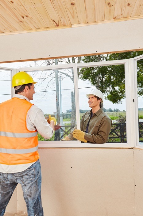 Dw&oacute;ch pracownik&oacute;w podczas montażu i uszczelniania plastikowego okna na placu budowy